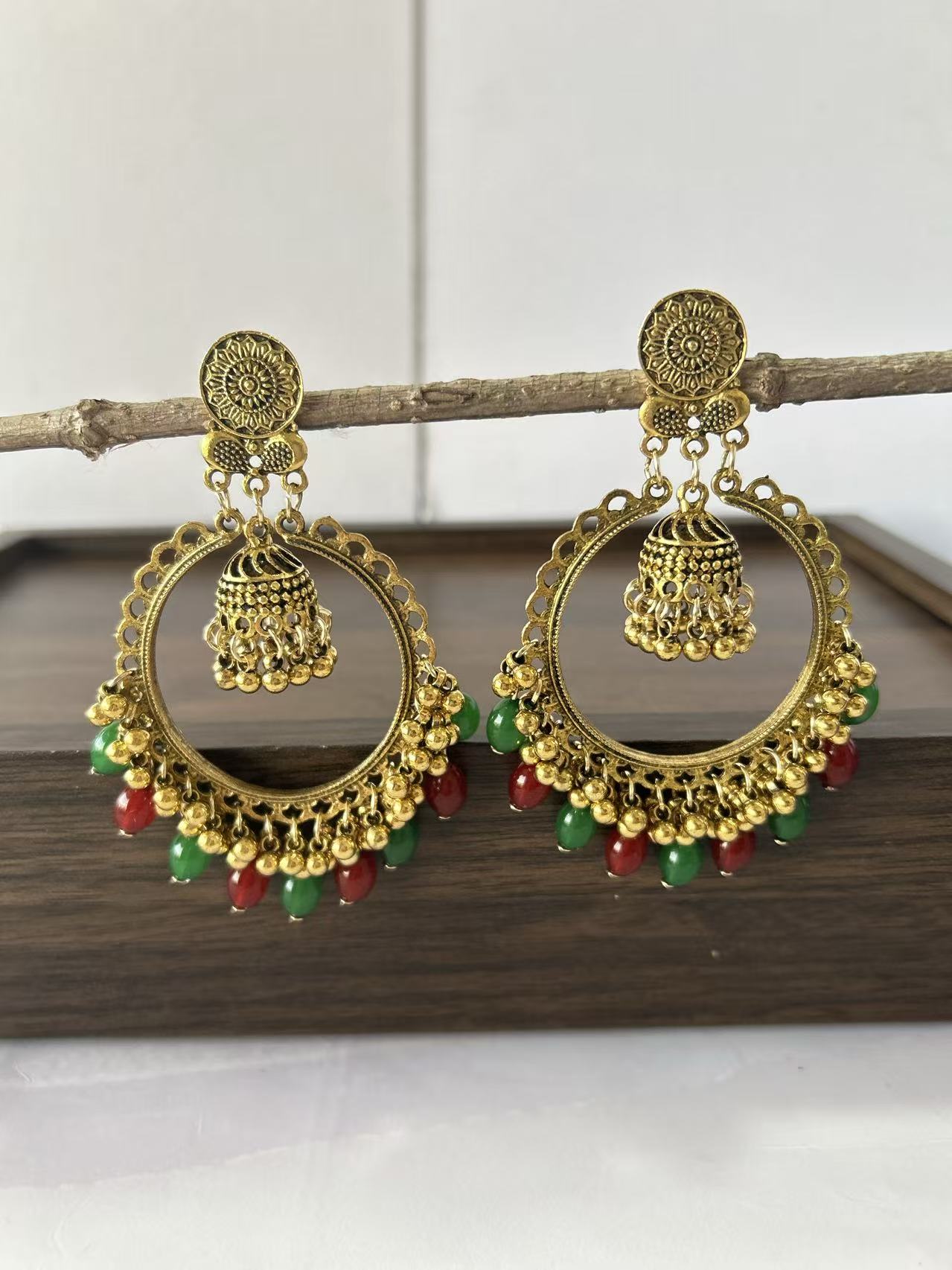 Gold earrings with green and red beads on a wooden surface